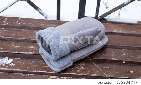 A pair of gray mittens with fur cuff on a wooden bench. Winter outdoor clothing for cold weather. Warm accessory for protection from frost and snow. A pair of gray mittens with fur cuff on a wooden bench. Winter outdoor clothing for cold weather. Warm accessory for protection from frost and snow. 135834747