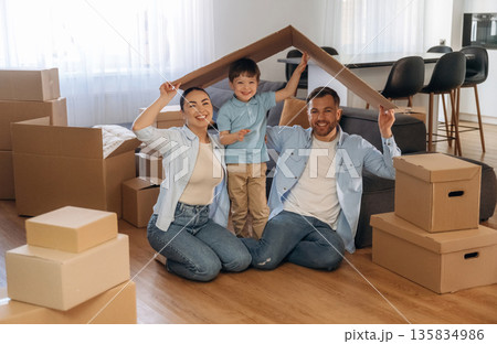 Playing with paper that is from the box. Family of husband, wife and son are moving into new house Playing with paper that is from the box. Family of husband, wife and son are moving into new house 135834986