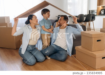 Front view, holding paper from box, sitting. Family of husband, wife and son are moving into new house Front view, holding paper from box, sitting. Family of husband, wife and son are moving into new house 135834995