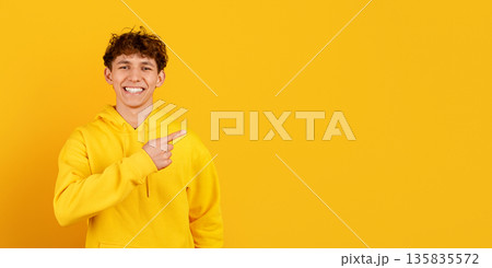 Happy guy in yellow hoodie pointing sideways at copy space, studio background Happy guy in yellow hoodie pointing sideways at copy space, studio background 135835572