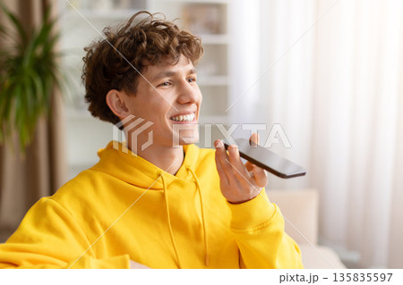 Young man in yellow hoodie using smartphone speakerphone at home 135835597