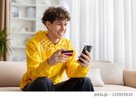 Teenage guy using smartphone and holding credit card at home Teenage guy using smartphone and holding credit card at home 135835610