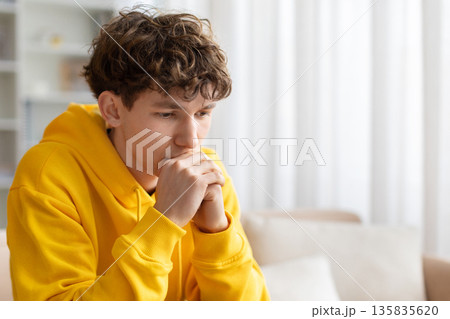 Thoughtful teenage boy sitting on sofa with hands near face 135835620