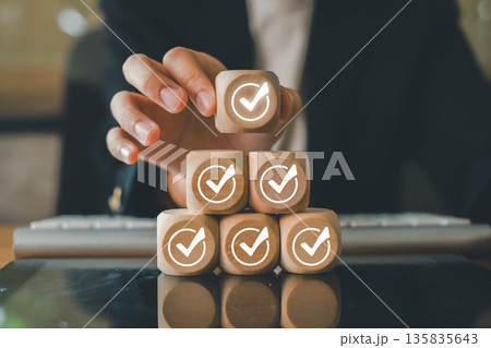 A professional arranges wooden blocks with checkmarks, representing success, goals, and achievement in a business environment. 135835643