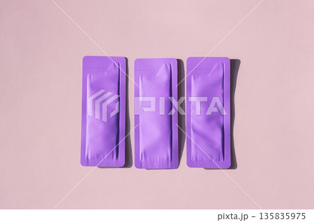 Three purple cosmetic sachet packets on light pink background. 135835975