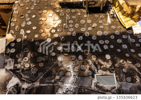 Severely fire damaged building with melted circular tiles, scorched window frame, collapsed roof, and distorted signage, revealing intense heat and structural devastation. 135836623