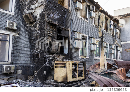 Charred wall, broken windows, and a scorched generator mark the aftermath of a fire, with debris scattered and air conditioners intact on the adjacent facade. 135836628
