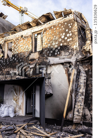 Charred building with scorched circular facade, collapsed roof, and blackened entrance shows severe fire damage; debris and white sacks lie near doorway, crane visible in background. Charred building with scorched circular facade, collapsed roof, and blackened entrance shows severe fire damage; debris and white sacks lie near doorway, crane visible in background. 135836629