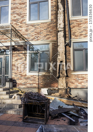 Charred vertical strip on brick wall marks fire path; broken window, scorched cabinet, and tangled wires lie amid debris in damaged urban setting. Charred vertical strip on brick wall marks fire path; broken window, scorched cabinet, and tangled wires lie amid debris in damaged urban setting. 135836630