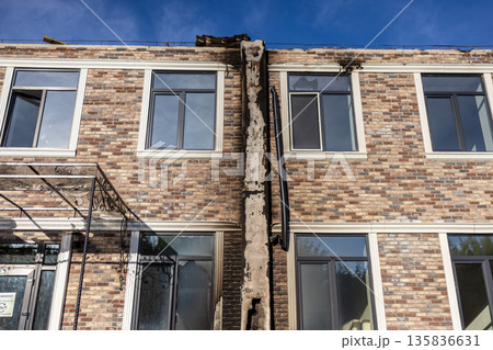 Two story brick building with charred central column and blackened roof shows fire path; intact windows bear soot stains, while decorative iron awning and broken panes hint at structural impact. 135836631
