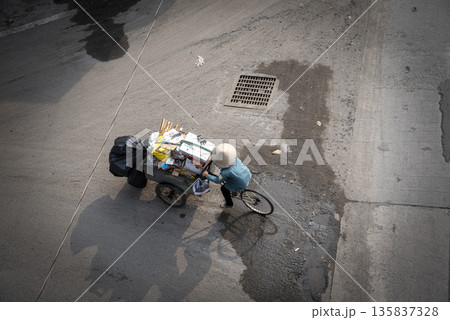 Man is riding a bicycle with a cart full of trash Man is riding a bicycle with a cart full of trash 135837328