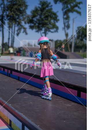 Child mastering roller skating on a skate park ramp while wearing protective equipment, focusing on coordination, control and safe movement during practice. Child mastering roller skating on a skate park ramp while wearing protective equipment, focusing on coordination, control and safe movement during practice. 135837617