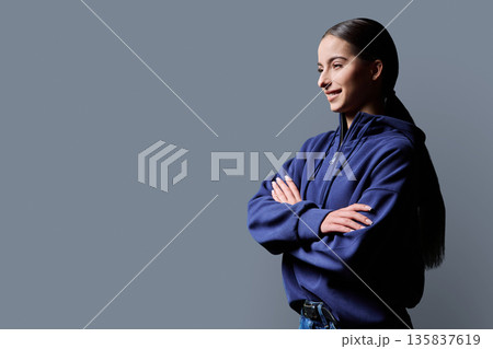 Profile view portrait of smiling teenage girl with crossed arms on grey background 135837619