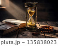 Hourglass measuring time beside old book and beads in historical interior 135838023