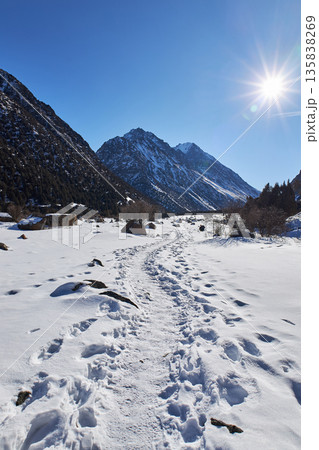 Footprints in snow leading through a winter mountain valley under a bright sun. Path through snowy landscape for travel or adventure concept. 135838269