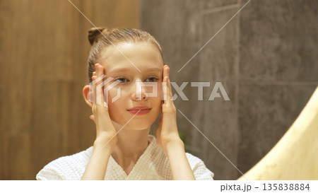 Caucasian teen girl enjoying skincare routine in bathroom, smiling while gently touching her face, promoting Skincare, Self care, and healthy skin. Caucasian teen girl enjoying skincare routine in bathroom, smiling while gently touching her face, promoting Skincare, Self care, and healthy skin. 135838884