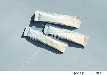 Three blank foil sachet packets on blue background with hard shadows 135838955