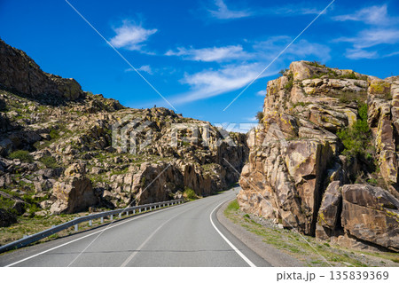 Asphalt road passing through stone cliffs at Stone Gates Chuysky Trakt Altai Russia. Iconic mountain pass framed by towering rocky formations. Asphalt road passing through stone cliffs at Stone Gates Chuysky Trakt Altai Russia. Iconic mountain pass framed by towering rocky formations. 135839369