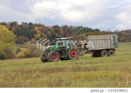 A tractor with a loaded trailer passes through a green field A tractor with a loaded trailer passes through a green field 135839602