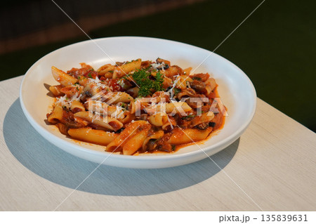 pasta spaghetti tossed chunky tomato-based sauce, mushroom and Cheese and vegetables on white ceramic plate, on wooden table, green leather chair background, food, health, copy space 135839631