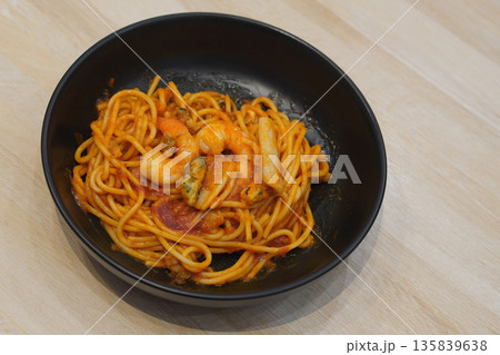 top view hot spaghetti with seafood, shrimp, tomato ketchup, cockles in a black ceramic bowl, on wooden floor background, food, object, copy space top view hot spaghetti with seafood, shrimp, tomato ketchup, cockles in a black ceramic bowl, on wooden floor background, food, object, copy space 135839638