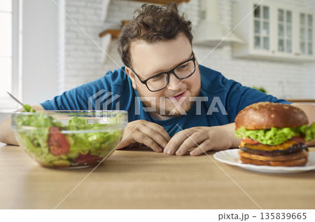 Hungry man choosing burger over salad, diet choice of funny overweight person Hungry man choosing burger over salad, diet choice of funny overweight person 135839665