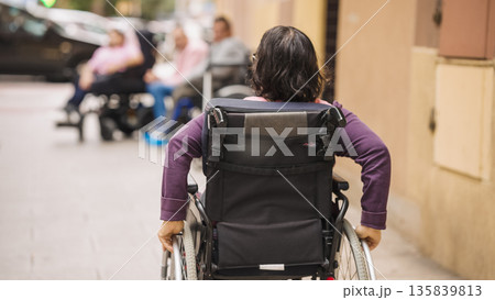 Person with disability pushing wheelchair on city street 135839813