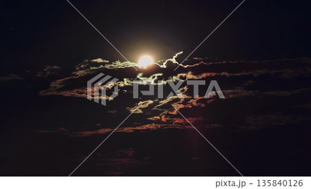 Full moon glowing behind dramatic clouds in dark night sky, creating mystical silhouette, natural dark background. Concept of cosmic mystery, celestial wonder, astrology, Halloween 135840126