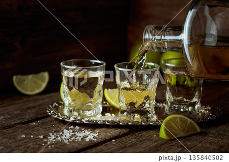Tequila with salt and lime slices on a silver tray. 135840502