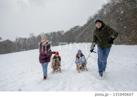 Parents pulling daughters on sled through winter landscape. Parents pulling daughters on sled through winter landscape. 135840687