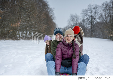 Family enjoying winter sledding together on snowy hill. 135840692