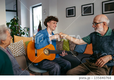 Young musician volunteer playing guitar for senirors in retirement home. Young musician volunteer playing guitar for senirors in retirement home. 135840768