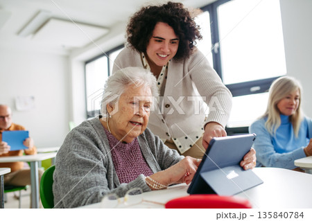 Elderly woman learning digital skills with tutor help. 135840784