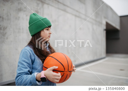 Sad girl alone in the city, want to play basketball. Young girl spending free time alone in the city, no friends, holding basketball. 135840800