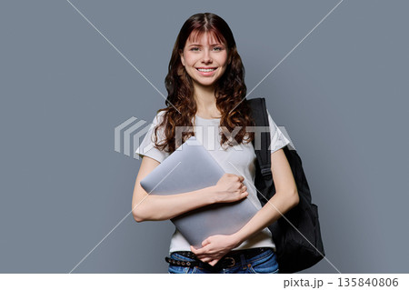 Portrait of beautiful girl teenage student holding laptop on gray background 135840806