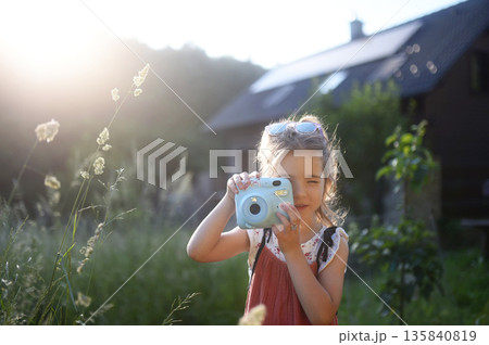 Little girl taking photos outdoors with instant camera. Little girl taking photos outdoors with instant camera. 135840819