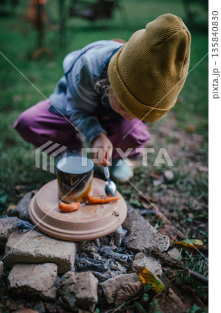 Little girl roasting vegetables on homemade campfire grill. Little girl roasting vegetables on homemade campfire grill. 135840830