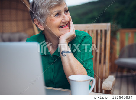 Mature woman sitting on balcony with laptop, working remotely. Mature woman sitting on balcony with laptop, working remotely. 135840834