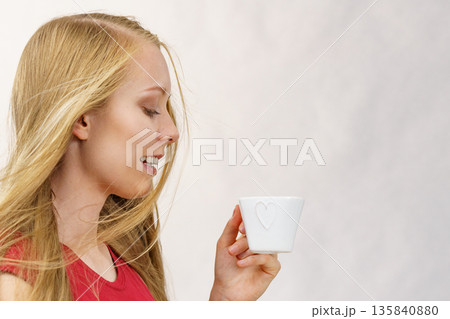 Blonde girl blowing hair holds coffee cup 135840880