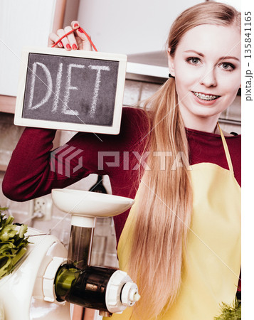 Woman in kitchen making vegetable smoothie juice Woman in kitchen making vegetable smoothie juice 135841165