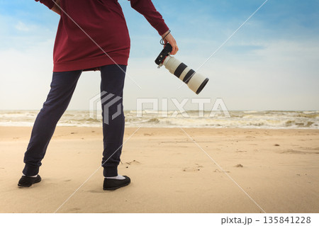 Woman walking on beach with camera 135841228
