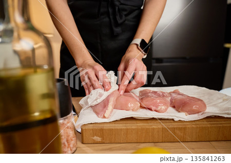 Woman drying raw chicken fillets with paper towels in home kitchen 135841263