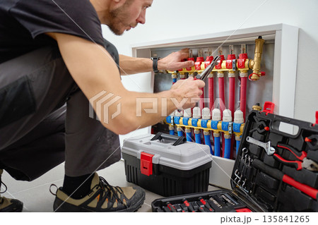 Technician adjusting underfloor heating manifold with valves and pipes 135841265