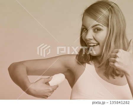 Girl applying stick deodorant in armpit. 135841282
