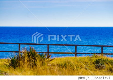 Seashore with fence and calm blue water 135841391