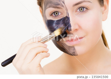 Female applying black mud facial mask Female applying black mud facial mask 135841500
