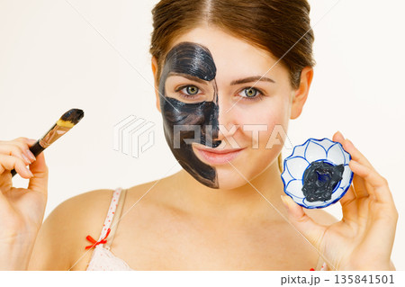 Female applying black mud mask to face Female applying black mud mask to face 135841501