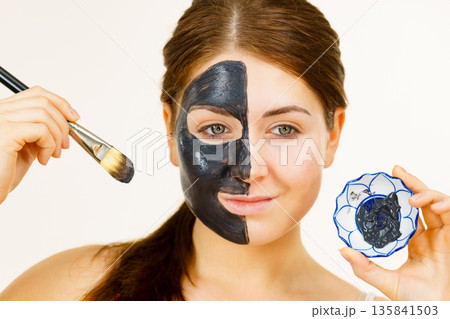 Female applying black mud mask to face 135841503