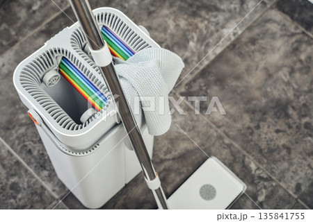 Cleaning supplies: mop, bucket with wringer sitting on tile floor in modern kitchen 135841755