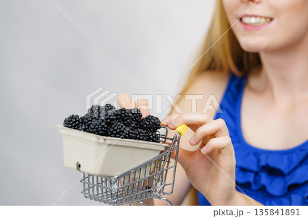 Girl holds blackberry fruits in shopping cart Girl holds blackberry fruits in shopping cart 135841891